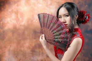 zuiden oosten- Aziatisch Chinese ras etnisch oorsprong vrouw vervelend rood fluweel cheongsam met hand- gestikt volgorde werk jurk kostuum hand- ventilator Aan retro wijnoogst achtergrond foto