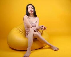 mooi jong zuiden oosten- Aziatisch vrouw zitten Aan een geel oranje zitzak stoel kleur achtergrond houding mode stijl elegant schoonheid humeur foto