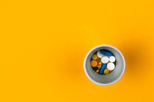 kleurrijke pillen of tabletten in glas op gele achtergrond foto