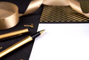 gouden pen lint paperclips en briefpapier op een zwarte achtergrond met een wit vel papier met kopie ruimte foto
