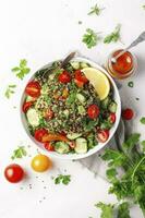 quinoa tabouleh salade met rood kers tomaten, oranje paprika, avocado, komkommers en peterselie. traditioneel midden- oostelijk en Arabisch gerecht. wit tafel achtergrond, top visie, genereren ai foto