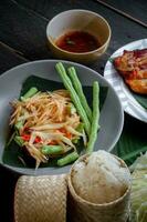 Thais voedsel schotel beide in Thailand en Azië, papaja salade of net zo wij telefoontje het somtum is aangevuld met gegrild kip en kleverig rijst- met vers roerbakgerechten. geserveerd Aan de zwart houten tafel. foto