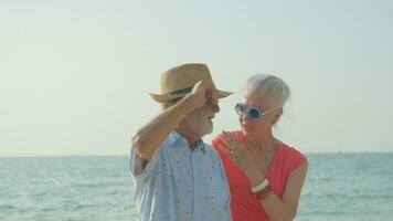 een ouderen paar knuffels hun schouders Bij de strand Aan hun zomer vakantie en ze glimlach en genieten hun vakantie. foto