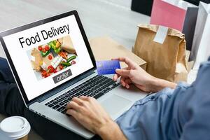 Mens bestellen nemen weg voedsel door internet met een laptop terwijl aan het liegen Bij huis. foto