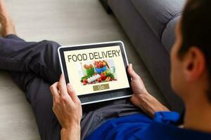 Mens bestellen nemen weg voedsel door internet met de tablet terwijl aan het liegen Bij huis. foto