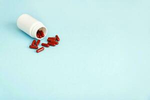 medisch capsules van rood kleur zijn gegoten uit van een vernietigd fles Aan een blauw achtergrond met kopiëren ruimte foto