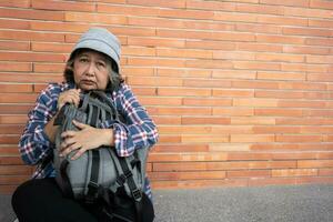 arm moe benadrukt depressief ouderen Aziatisch vrouw dakloos zittend Aan de straat in de schaduw van de gebouw en bedelen voor helpen en geld, ouderen Aziatisch vrouw verlaten concept foto