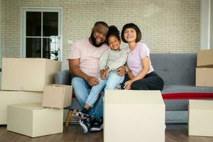 gemengd ras gezinnen zijn zittend Aan de sofa voor rust uit na in beweging naar een nieuw huis Aan de eerste dag na buying echt landgoed. concept van beginnend een nieuw leven voor een nieuw familie. foto