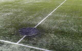 een gat in de grond van een kanon schelp explosie gevulde met vers aarde Bij een Amerikaans voetbal stadion. beschietingen krater in de stad. speelplaats. oorlog in Oekraïne. verwoesting van burger infrastructuur. foto