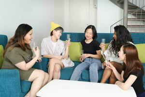 jong Aziatisch vrouw groep praten roddel babbelen zingen drinken proost partij pret genieten emotie Aan blauw leven kamer sofa foto