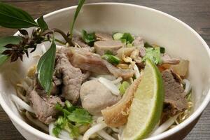 Vietnamees poh rundvlees noedels soep bouillon met rundvlees bal borst pens maag onderdelen geweest spruit Thais basilicum limoen in kom Aan houten tafel foto