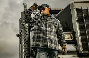 Kaukasisch Amerikaans vrachtwagenchauffeur in voorkant van zijn zwart semi vrachtauto trekker foto