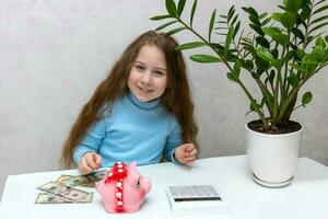 schattig gelukkig meisje Bij de tafel met geld, varkentje bank en rekenmachine foto