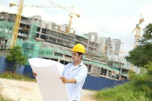 Aziatisch Mens Maleis arbeider ingenieur beheer moeilijk hoed veiligheid helm Bij bouw plaats lezing zien plan blauwdruk foto