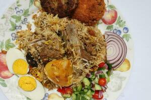 huis stijl schapenvlees kacchi biryani met aardappel karbonade tomaat komkommer ui salade Aan oud stijl bord over- wit achtergrond foto