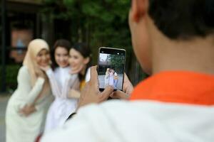 groep jong Aziatisch Chinese Maleis Mens vrouw vervelend hoofddoek buitenshuis vriend leerling collega gelukkig nemen foto portret door hand- telefoon slim telefoon scherm