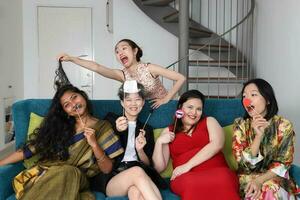 jong Aziatisch vrouw groep praten zingen maken grappig spottend gezichten uitdrukking selfie portret papier rekwisieten snor hoed pijp neus- haar- Aan blauw leven kamer sofa zitten foto