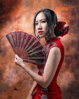 zuiden oosten- Aziatisch Chinese ras etnisch oorsprong vrouw vervelend rood fluweel cheongsam met hand- gestikt volgorde werk jurk kostuum hand- ventilator Aan retro wijnoogst achtergrond foto