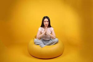 mooi jong zuiden oosten- Aziatisch vrouw zit Aan een geel zitzak stoel oranje geel kleur achtergrond houding mode stijl elegant schoonheid humeur uitdrukking rust uit kom tot rust oefening rekken yoga foto