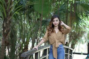 jong Aziatisch Maleis vrouw buitenshuis groen Aan houten brug houding foto