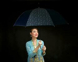 Aziatisch vrouw in trekkracht kebaya draag- paraplu Aan zwart achtergrond foto