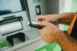 Mens Geldautomaat kaart. Geldautomaat insert kaart. Mens zetten credit kaart in Geldautomaat machine terwijl Holding portemonnee foto
