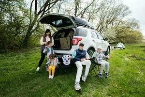 moeder met kinderen zitten Aan stoel tegen auto Aan picknick. foto