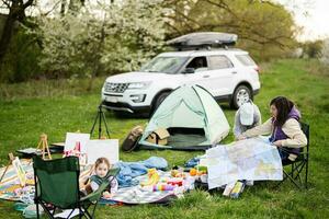 moeder houden Europa kaart, met kinderen zitten Aan stoel tegen auto Aan picknick. foto