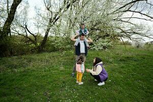 familie met twee dochters in voorjaar weide Aan de achtergrond van een bloeiend boom. foto