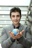 midden- oostelijk Kaukasisch jong kantoor bedrijf Mens vervelend pak Holding wereldbol wereld kaart Aan palm van zijn hand- Bij buitenshuis gebouwen foto