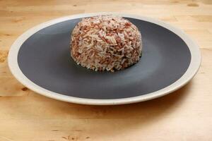 nasi dagang speciaal bruin wit rijst- gekookt met kokosnoot melk en kruid Aan zwart uit wit rand bord Aan houten achtergrond foto