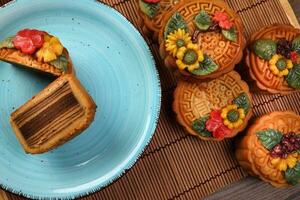 kleurrijk bloem versierd mooncake Chinese midden herfst festival besnoeiing plak Aan blauw keramisch bord achtergrond Aan bamboe voedsel mat foto