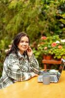 een vrouw met een kop van koffie en een laptop zit Bij een tafel in een serre. freelancer, bloemist. foto