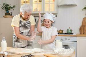 gelukkig familie in keuken. grootmoeder en kleindochter kind koken in keuken samen. grootmoeder onderwijs kind meisje kneden deeg bakken koekjes. huishouden samenspel helpen familie generaties concept. foto