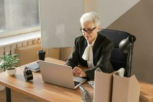 zelfverzekerd elegant Europese midden- oud senior vrouw gebruik makend van laptop Bij werkplek. elegant ouder volwassen Jaren 60 grijs haren dame zakenvrouw zittend Bij kantoor tafel. baas leider leraar professioneel arbeider. foto