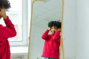 liefde jezelf. mooi jong glimlachen Afrikaanse Amerikaans vrouw dansen aanraken gekruld haar- genieten van haar spiegel reflectie. zwart dame op zoek Bij spiegel op zoek zelfverzekerd en gelukkig. zelf liefde concept. foto