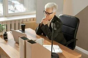 zelfverzekerd elegant Europese midden- oud senior vrouw gebruik makend van laptop Bij werkplek. elegant ouder volwassen Jaren 60 grijs haren dame zakenvrouw zittend Bij kantoor tafel. baas leider leraar professioneel arbeider. foto