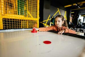 schattig kleuter meisje spelen lucht hockey Bij kinderen Speel centrum. foto