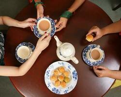 top visie van thee drinken partij vrouw handen gieten sharing theepot theekopje schotel traditioneel biscuit Aziatisch jurk foto