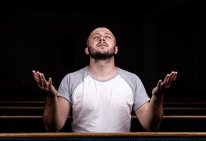een christelijke man in een wit overhemd zit met zijn handen omhoog en bidt met nederig hart in de kerk foto