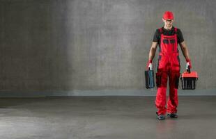 bouw arbeider in rood uniform wandelen met gereedschapskisten in zijn handen foto