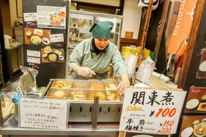 osaka, Japan, 2018- Japans vrouw handelaar en haar Japans tussendoortje winkel. het is een voedsel dat combineert een verscheidenheid van voedingsmiddelen en populair naar gegeten in de winter. foto