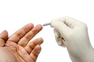 hand- van dokter in wit medisch handschoen Holding bloed lancet steken Aan menselijk midden- vinger naar controleren glucose in de bloed isoleren Aan wit achtergrond en maken met paden. foto