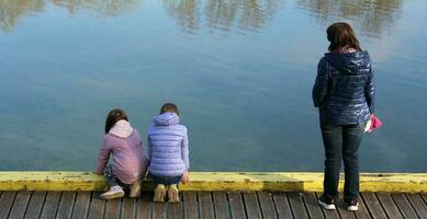 Sankt petersburg Rusland - 05 10 2023 mam met twee zonen zittend Aan houten pier aan het kijken eenden foto