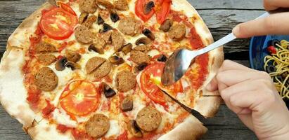 dichtbij omhoog mensen hand- gebruik lepel en hand- aan het eten peperoni pizza met spaghetti en ketchup Aan houten tafel Bij restaurant. Italiaans voedsel en gewricht partij samen foto