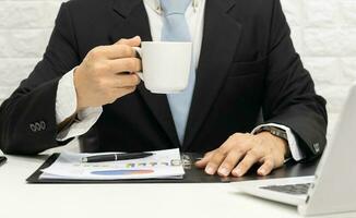 zakenman uitvoerend werken Aan laptop Bij zijn bureau en drinken koffie. foto