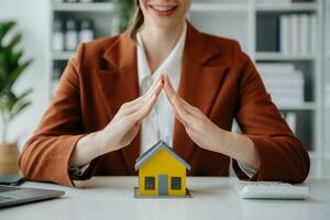 vrouw echt landgoed middel is gebruik handen naar beschermen rood dak voor de concept van echt landgoed investering over huis handel, aankoop Bij bureau in kantoor foto