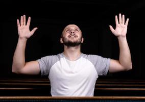 een christelijke man in een wit overhemd zit met zijn handen omhoog en bidt met nederig hart in de kerk foto