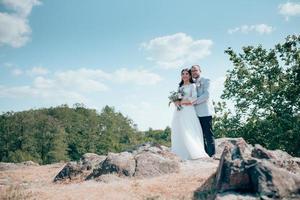 trouwfoto van de bruid en bruidegom in een grijsroze kleur op de natuur in het bos en de rotsen