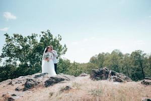 trouwfoto van de bruid en bruidegom in een grijsroze kleur op de natuur in het bos en de rotsen
